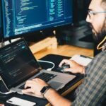 Software developer writing code on two screens